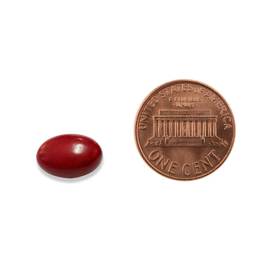 A red softgel capsule being compared to the size of a penny