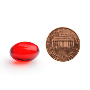 A clear red softgel capsule being compared to the size of a penny