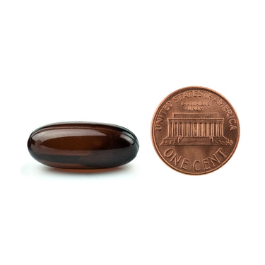 A brown softgel capsule being compared to the size of a penny
