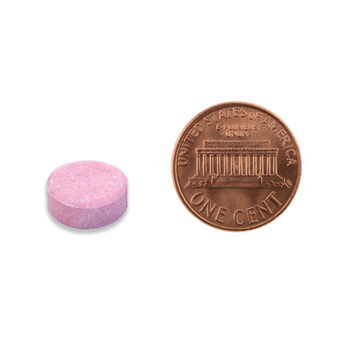 A pink tablet being compared to the size of a penny