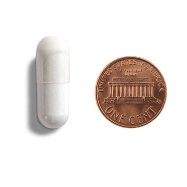 A white cdapsule being compared to the size of a penny