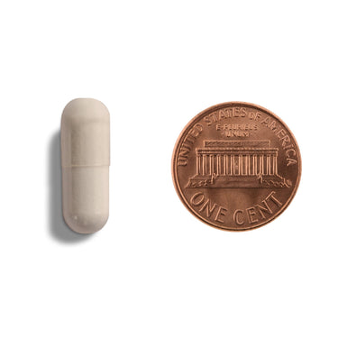 An off-white capsule being compared to the size of a penny