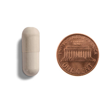 An off-white capsule being compared to the size of a penny